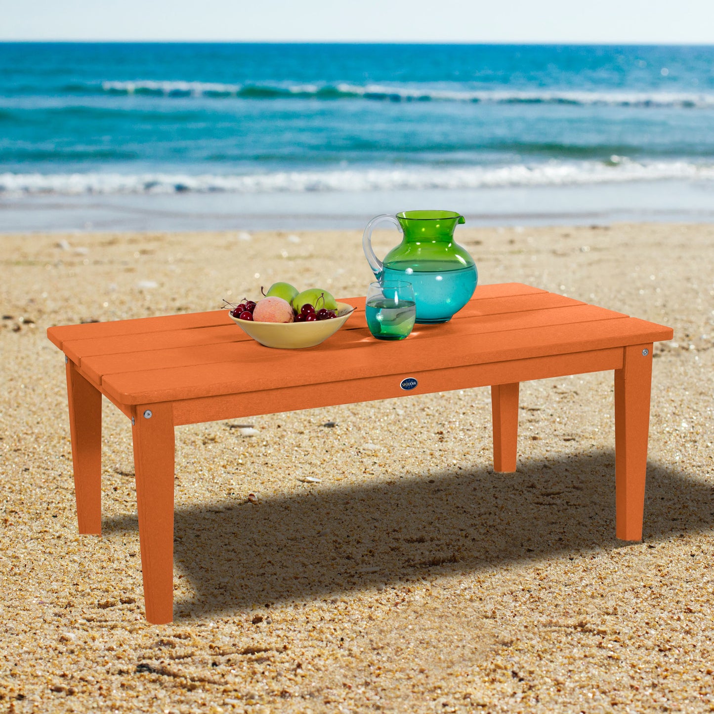 Orange Sunrise Coast conversation table on beach with water pitcher and fruit