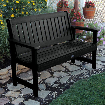 5ft black Blue Ridge garden bench on stone pathway with flowers in background 