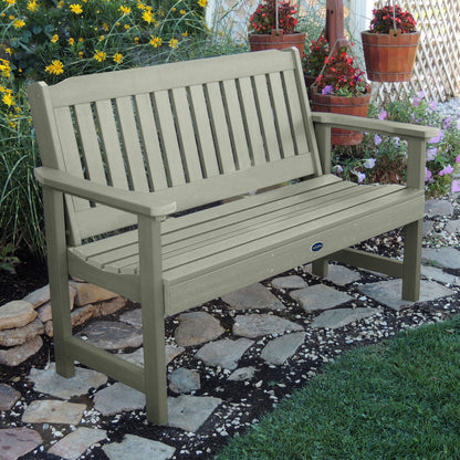 5ft light green Blue Ridge garden bench on stone pathway with flowers in background 