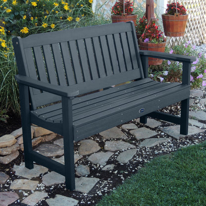 5ft dark blue Blue Ridge garden bench on stone pathway with flowers in background 