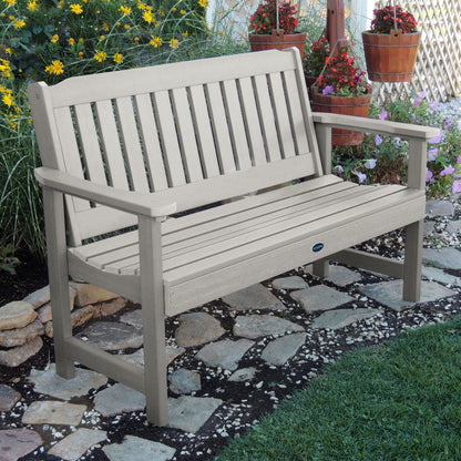 5ft light gray Blue Ridge garden bench on stone pathway with flowers in background 