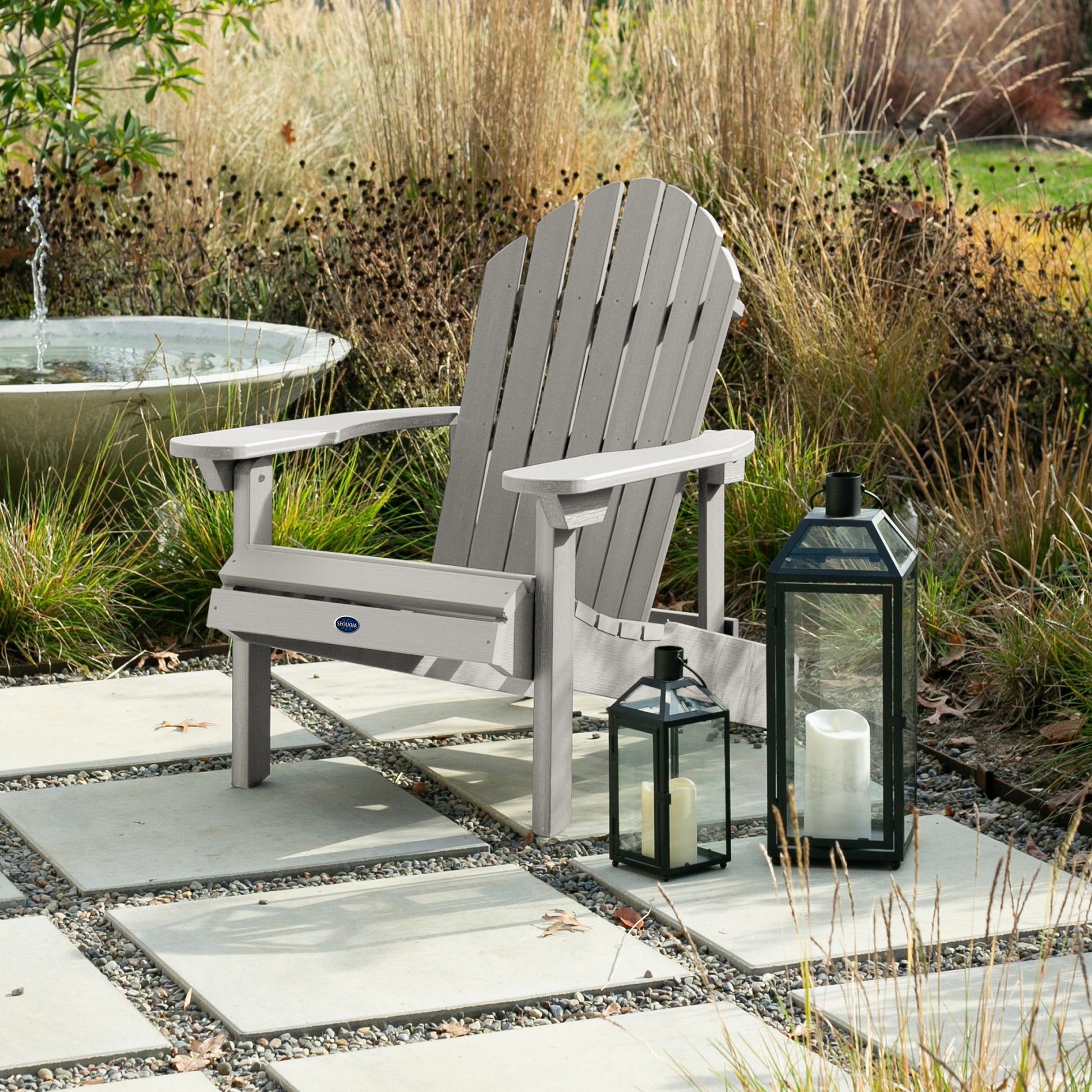 Light gray Horizon Adirondack chair on stone next to lanterns