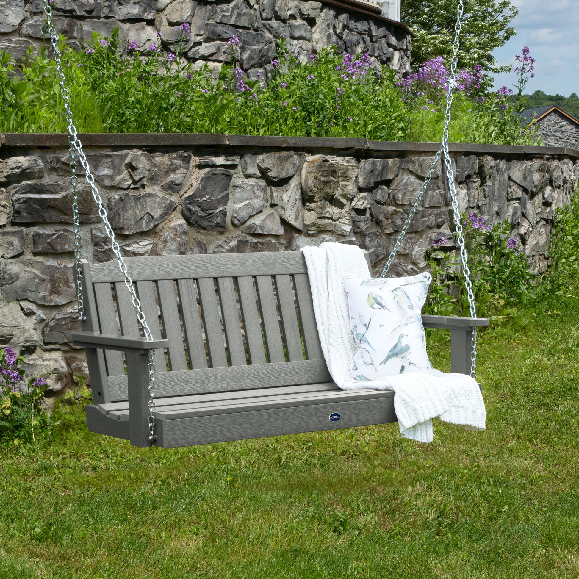 Gray 4ft Blue Ridge porch swing with blanket and pillow and stone wall in background