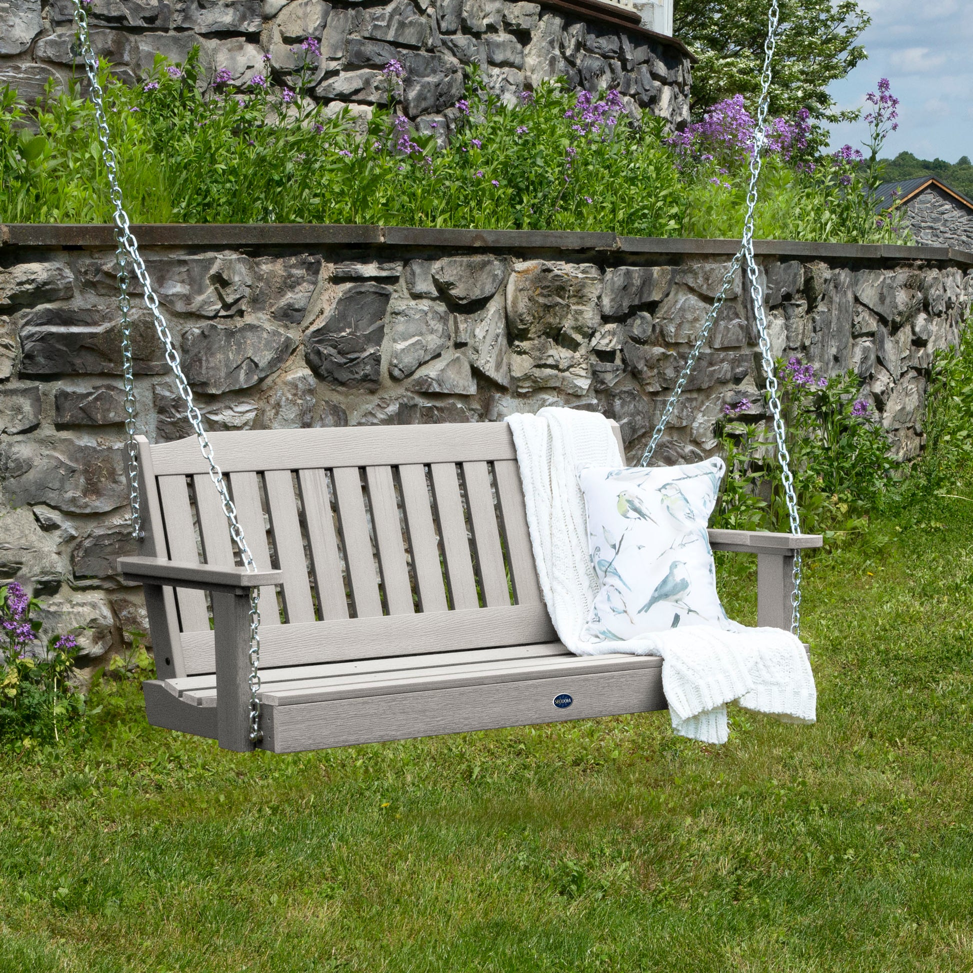 Light gray 4ft Blue Ridge porch swing with blanket and pillow and stone wall in background