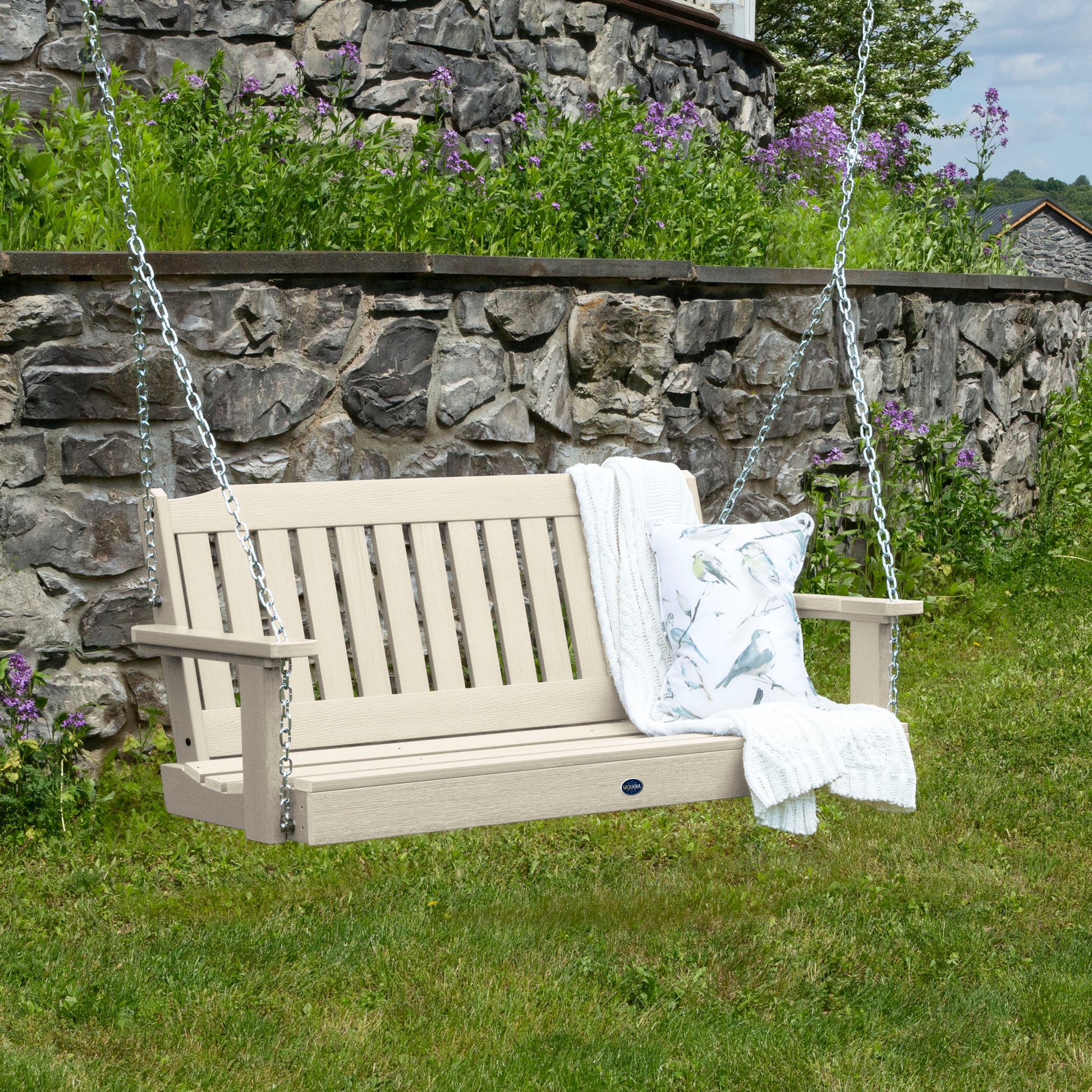 Whitewash 4ft Blue Ridge porch swing with blanket and pillow and stone wall in background