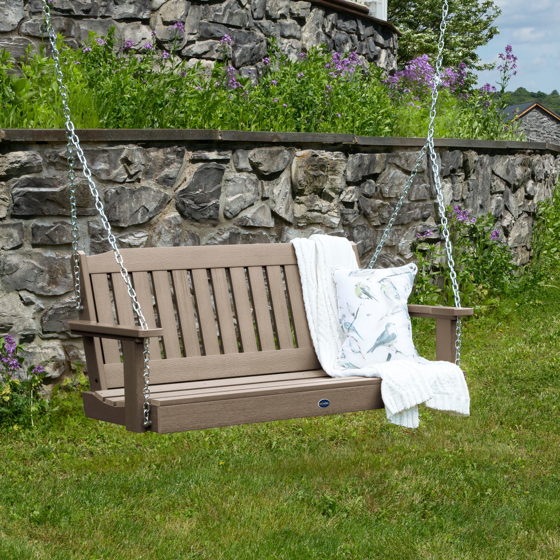 Light brown 4ft Blue Ridge porch swing with blanket and pillow and stone wall in background