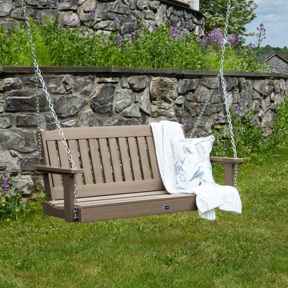 Light brown 4ft Blue Ridge porch swing with blanket and pillow and stone wall in background