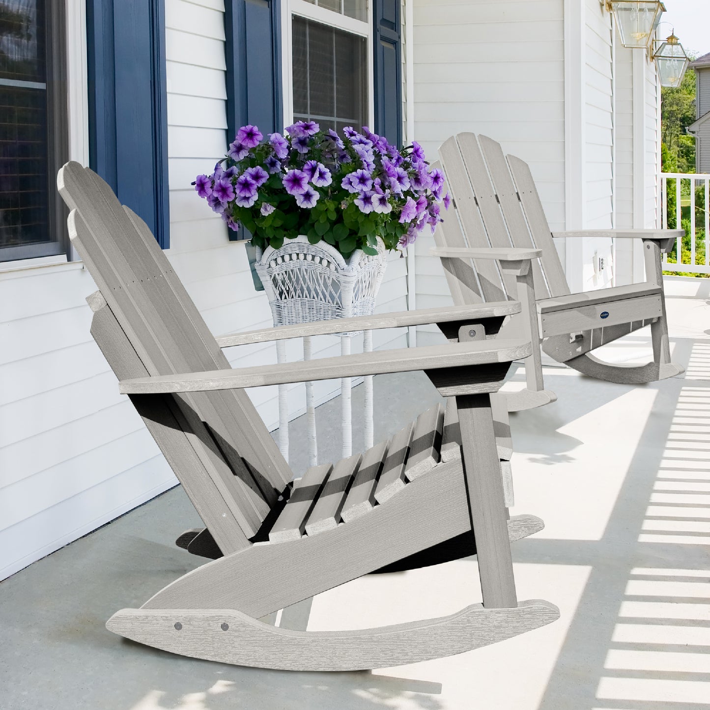 Two light gray Lighthouse Adirondack rocking chairs on front porch with flowers