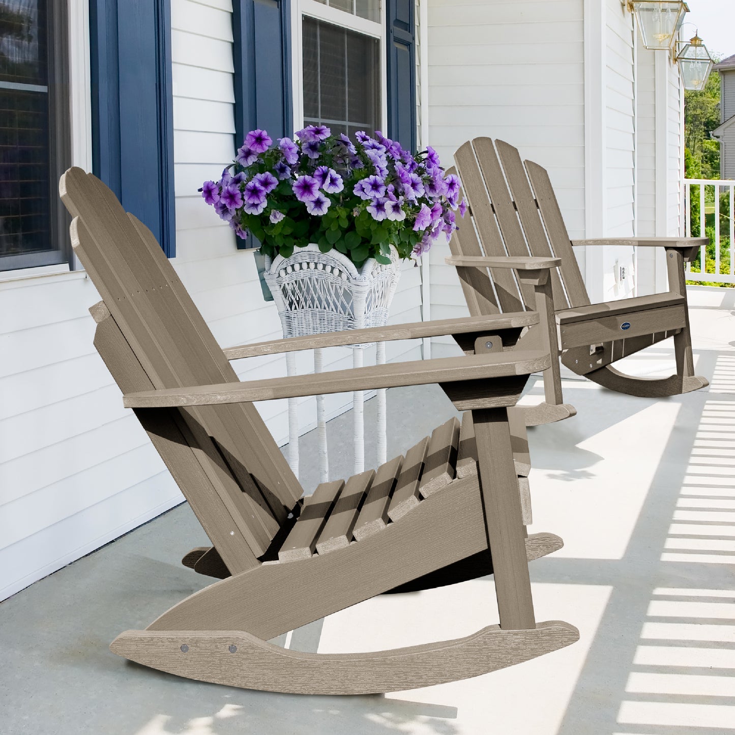 Two light brown Lighthouse Adirondack rocking chairs on front porch with flowers