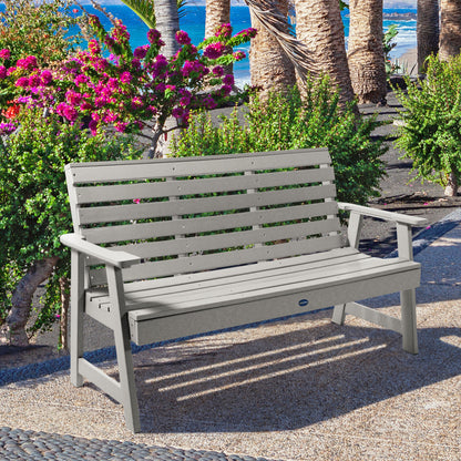 Gray Sunrise Coast 5ft bench in front of flowers on walkway