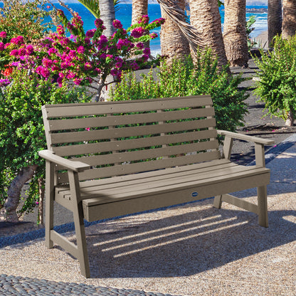 Tan Sunrise Coast 5ft bench in front of flowers on walkway