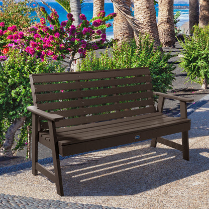 Brown Sunrise Coast 5ft bench in front of flowers on walkway