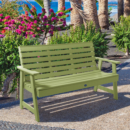 Green Sunrise Coast 5ft bench in front of flowers on walkway