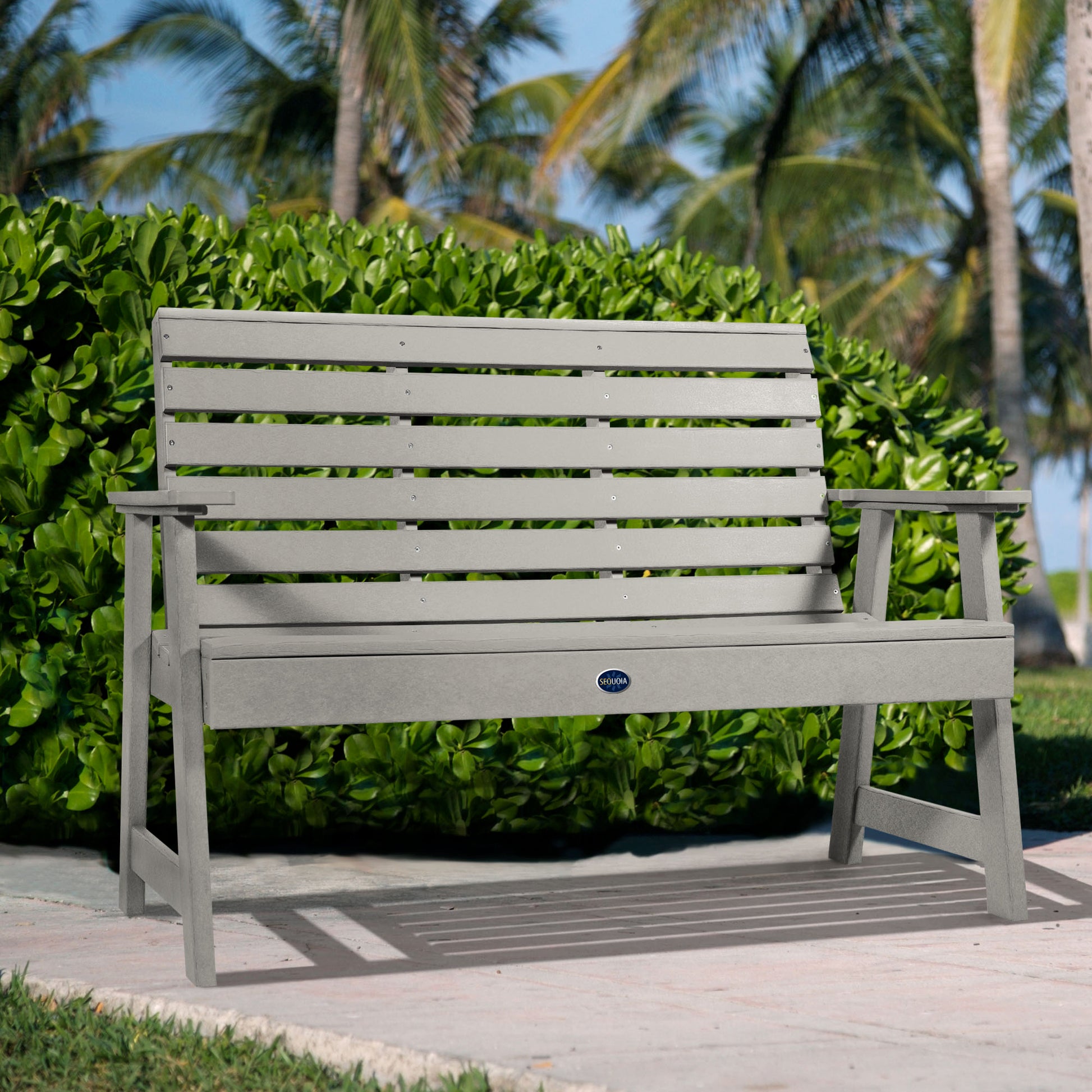 Gray Sunrise Coast 4ft bench in front of bush on walkway