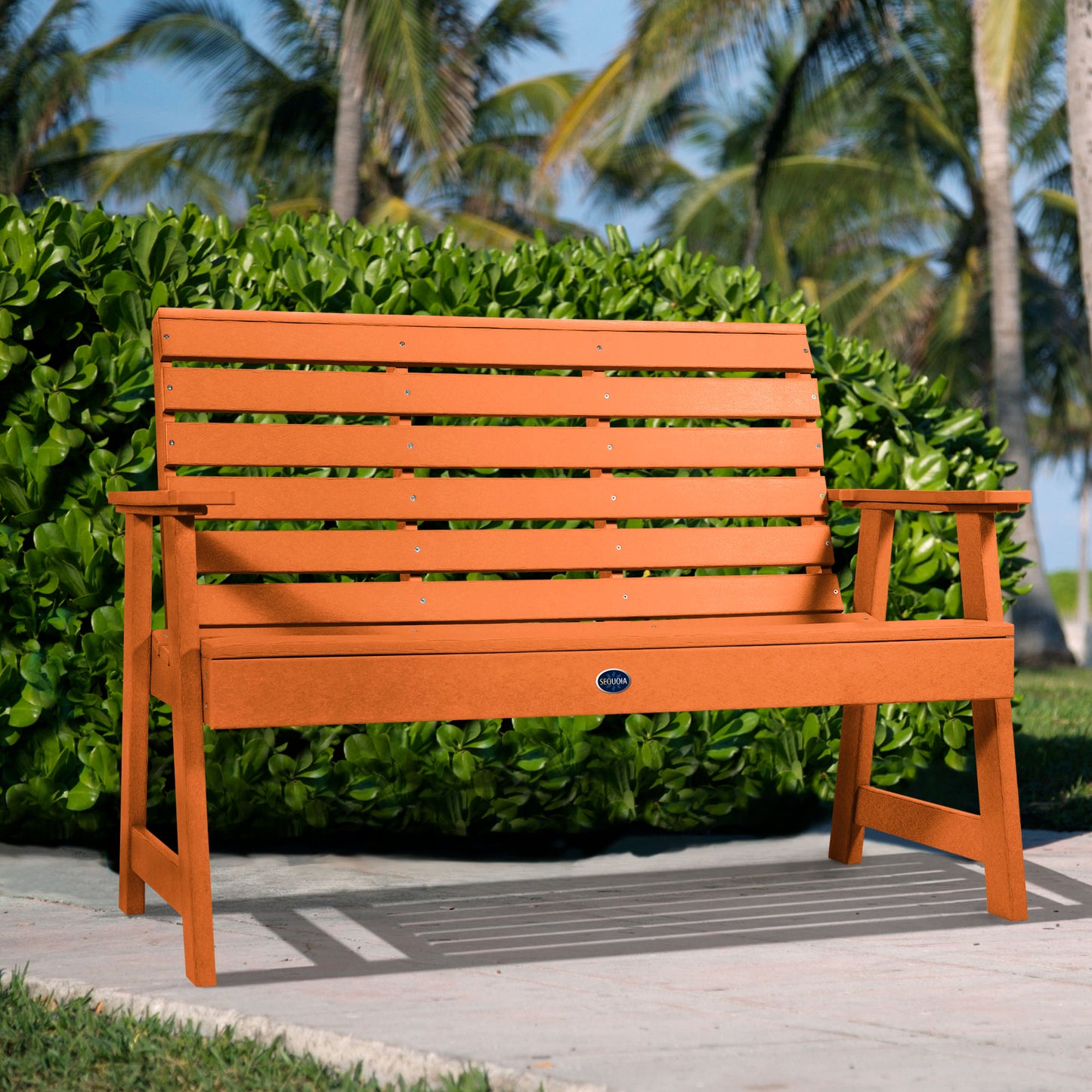 Orange Sunrise Coast 4ft bench in front of bush on walkway