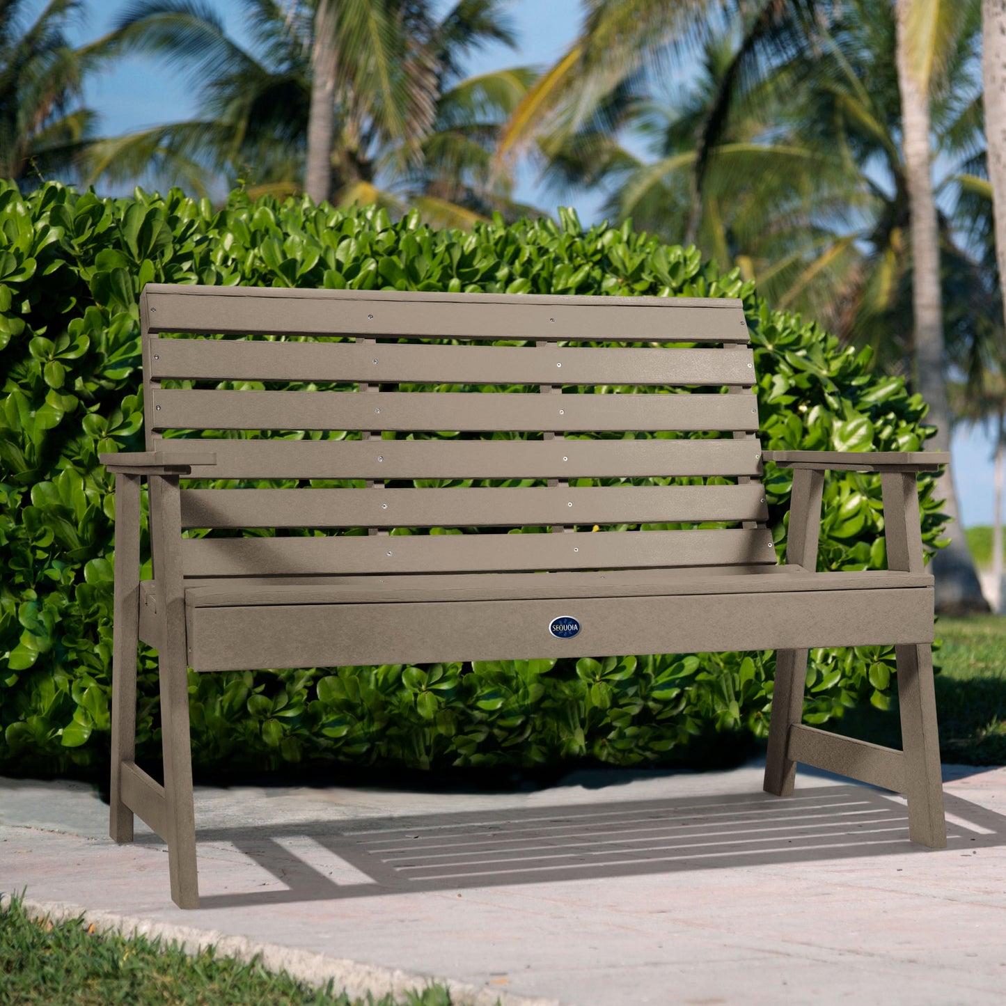 Tan Sunrise Coast 4ft bench in front of bush on walkway