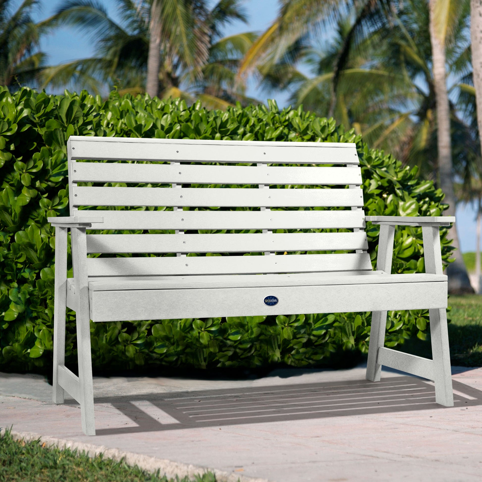 White Sunrise Coast 4ft bench in front of bush on walkway