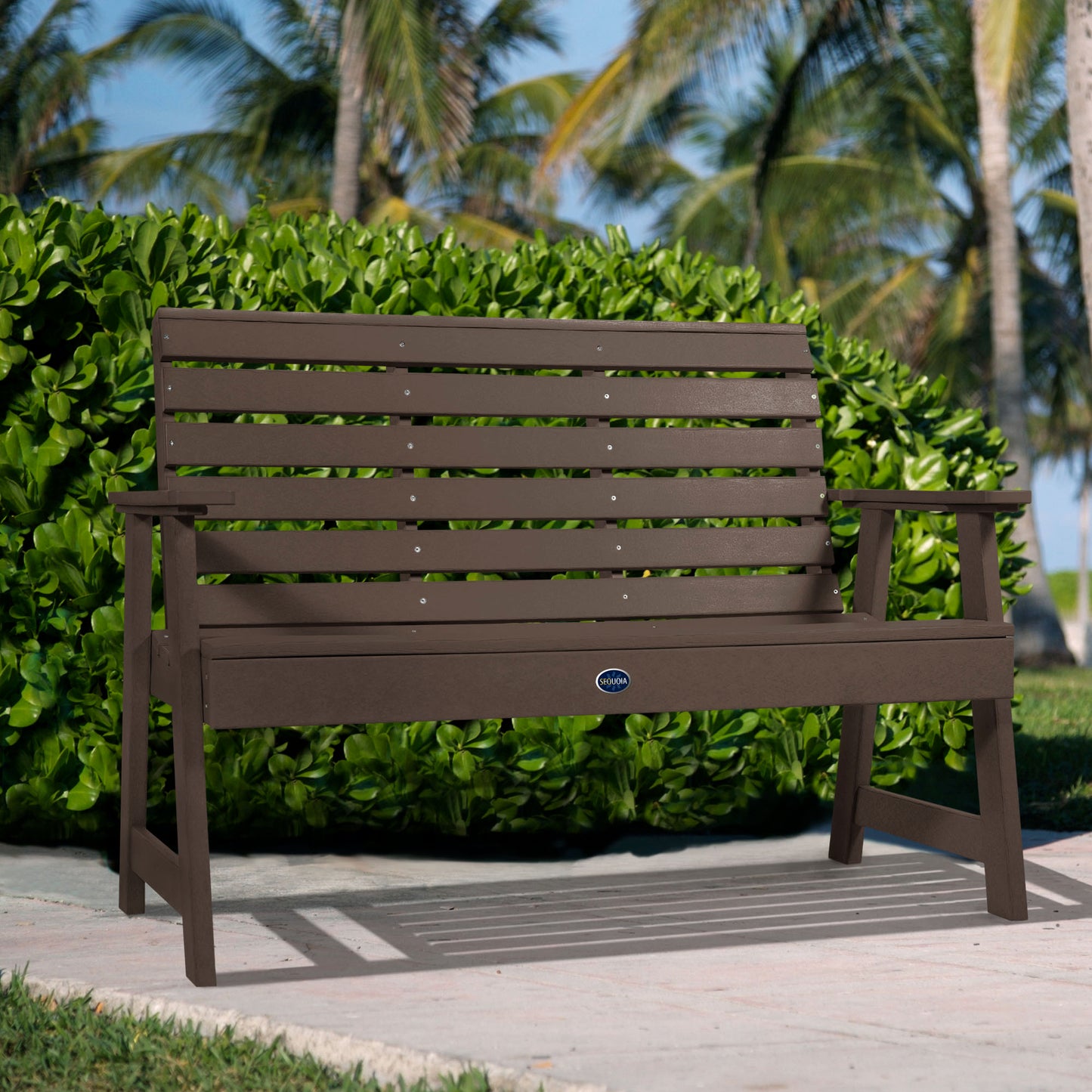 Brown Sunrise Coast 4ft bench in front of bush on walkway