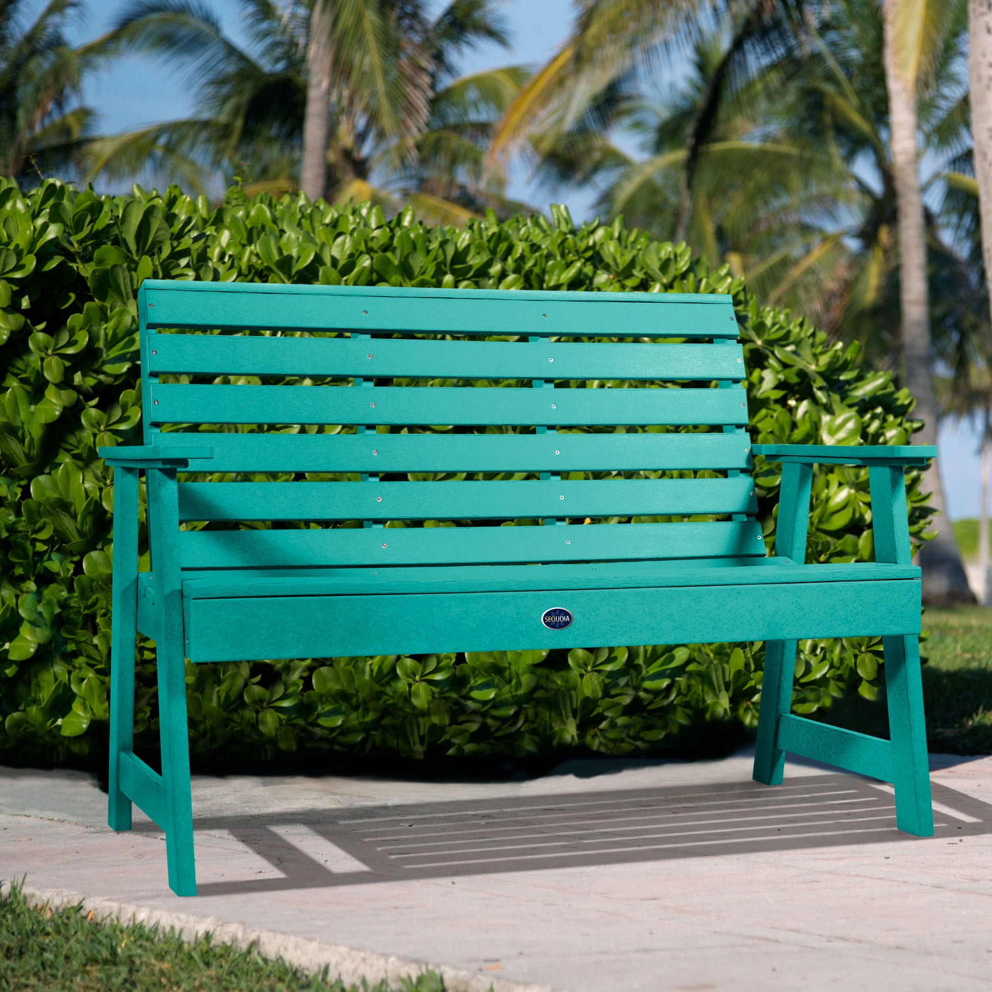 Blue Sunrise Coast 4ft bench in front of bush on walkway